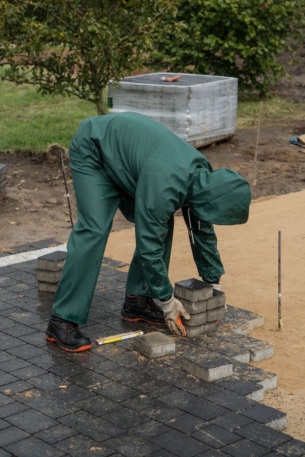 Worker wearing rain gear setting dark concrete pavers at a construction site