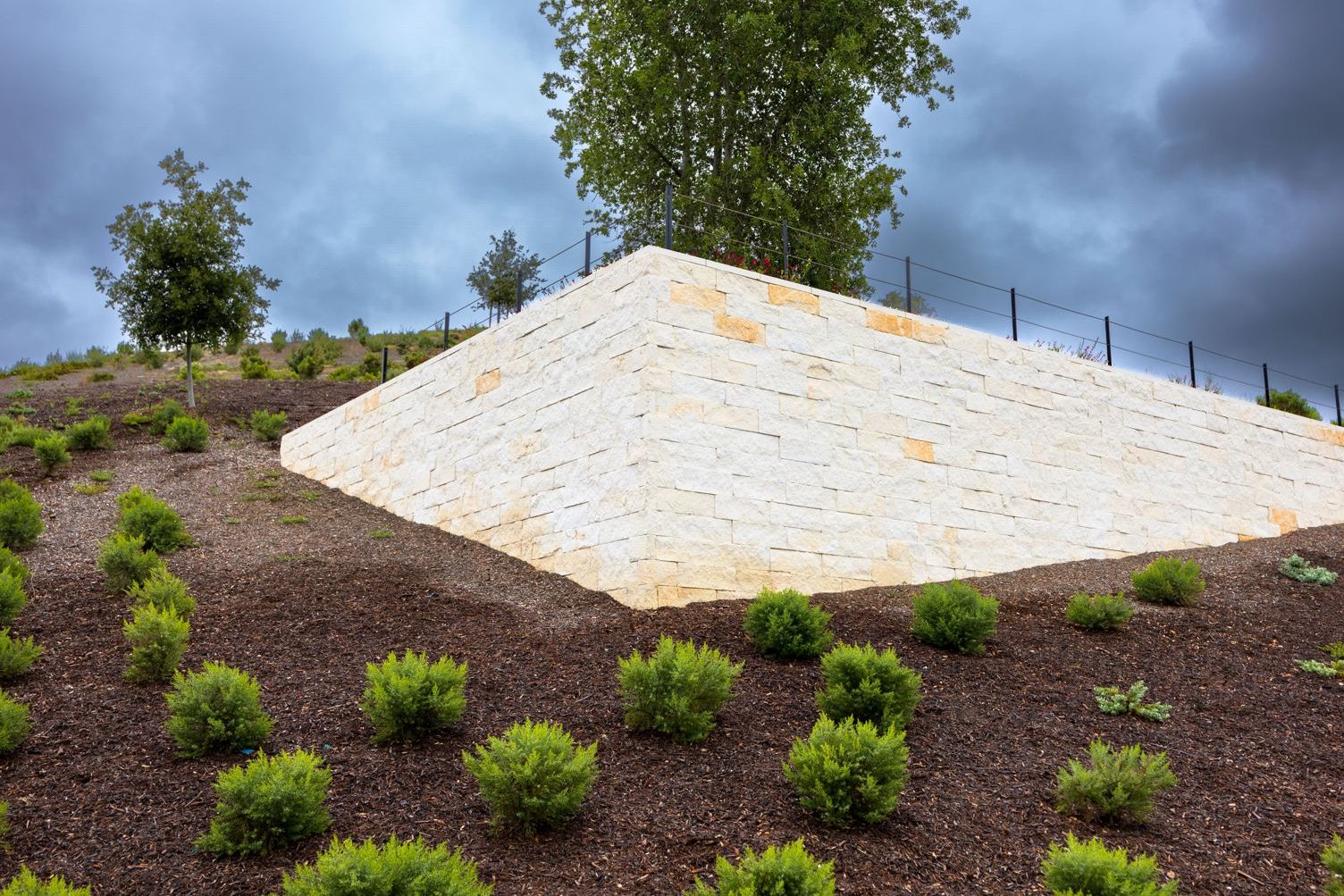 High stacked stone retaining wall holding back a sloped hillside under a cloudy sky