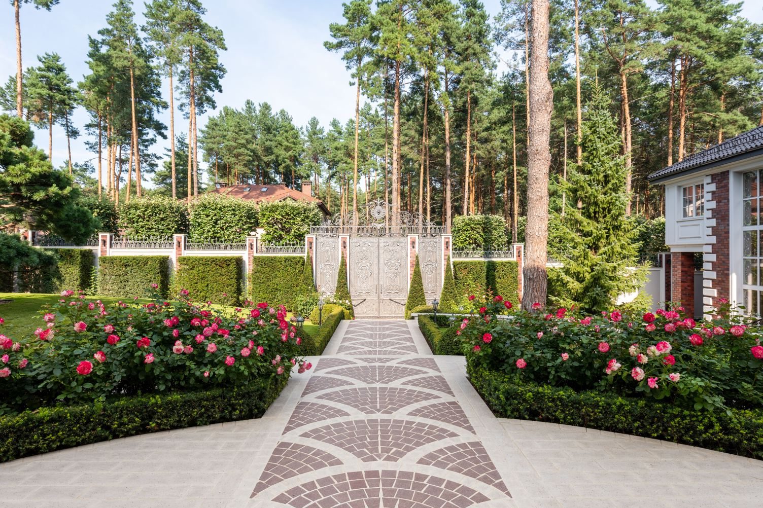 Rose bushes and trimmed hedges along a paver walkway leading to a decorative gate