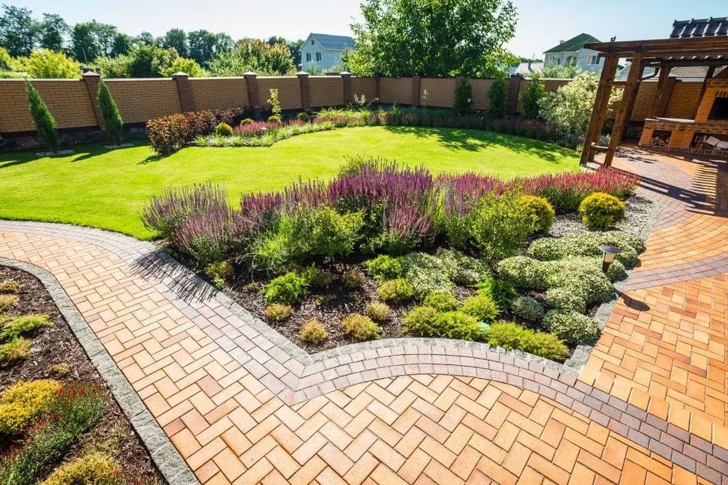 Herringbone brick patio wrapping a round lawn with planting beds and a pergola