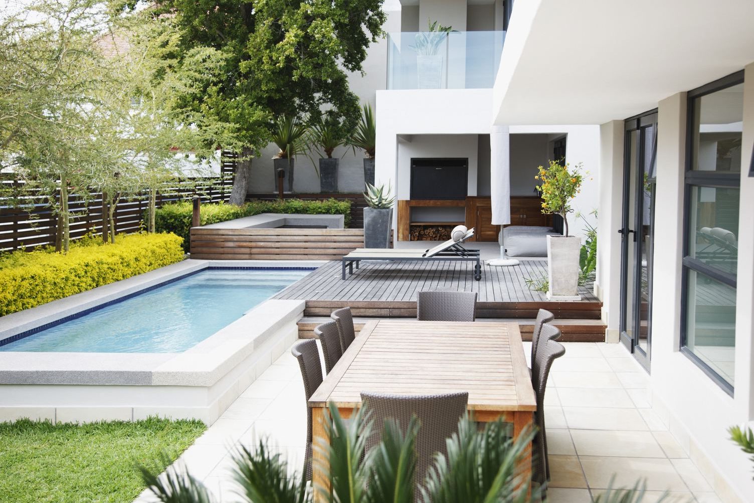 Backyard with a wood deck, a dining table, and a pool next to a covered outdoor lounge area