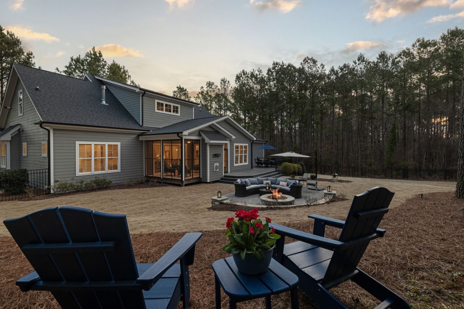 Patio at dusk with a lit fire pit, seating, and Adirondack chairs