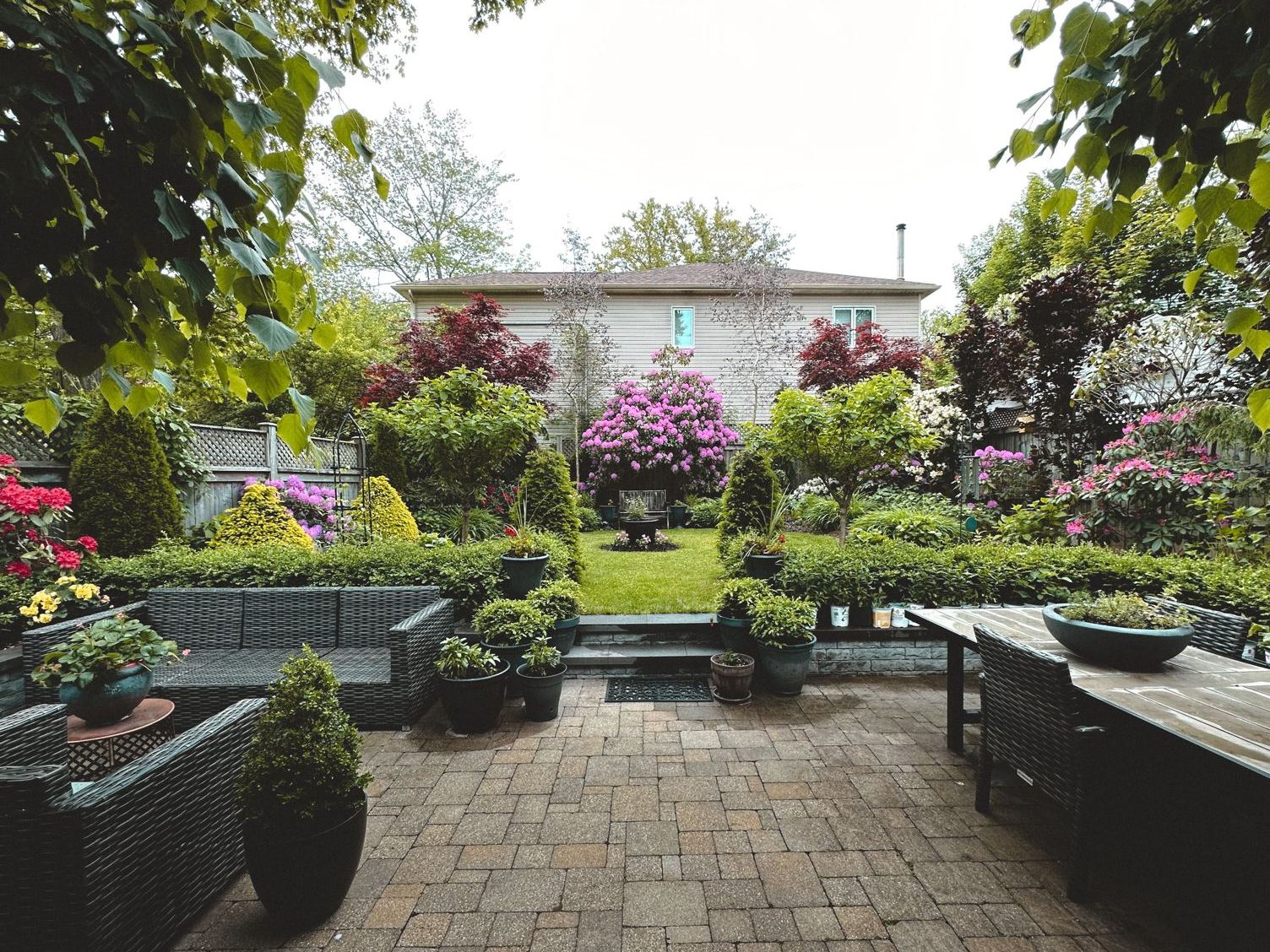 Paver patio under a pergola with a dining table and bright flower beds