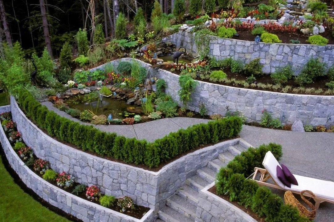Stepped stone retaining walls terracing a garden beside a small pond