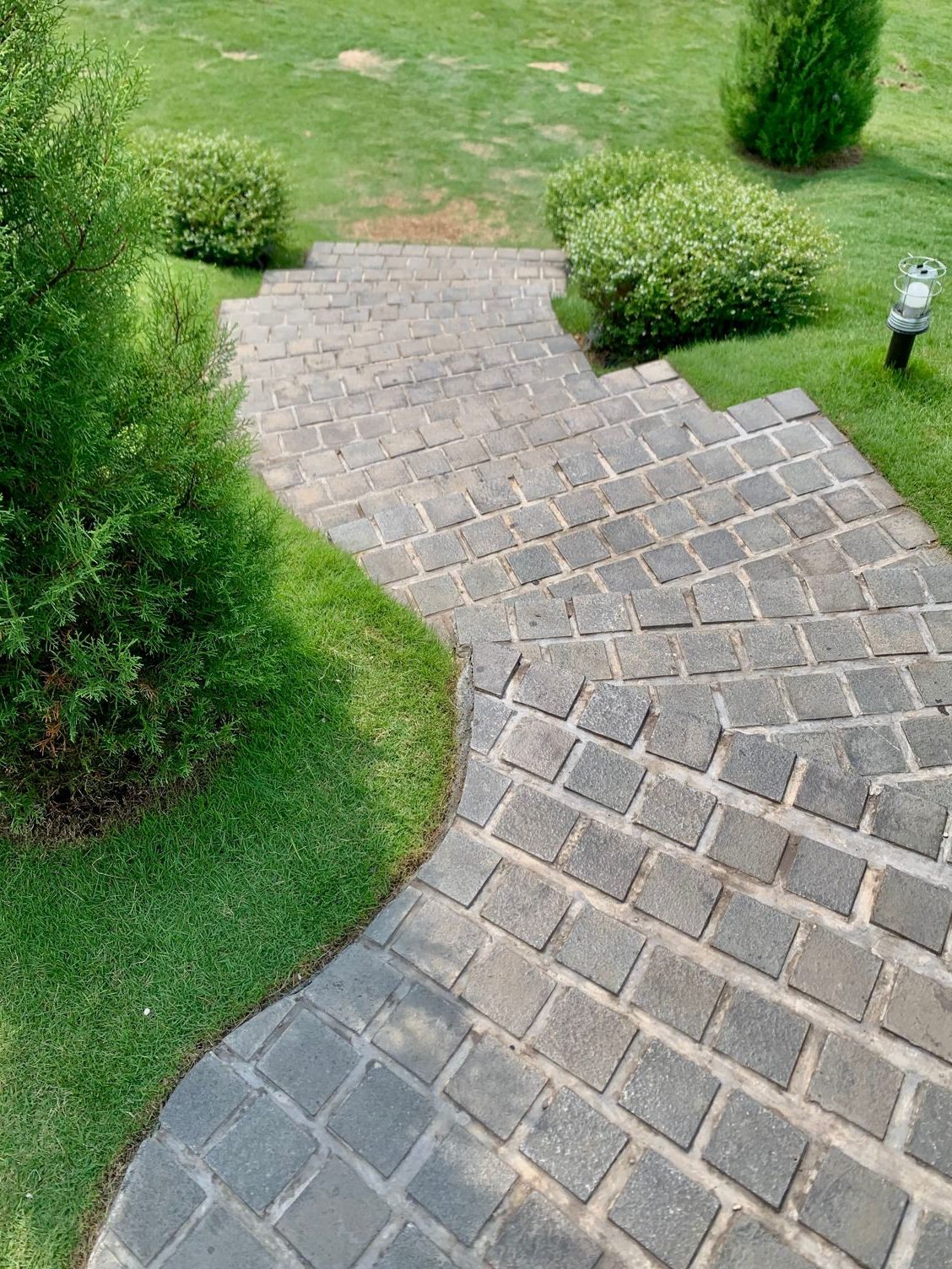 Herringbone brick walkway curving across a well-kept lawn