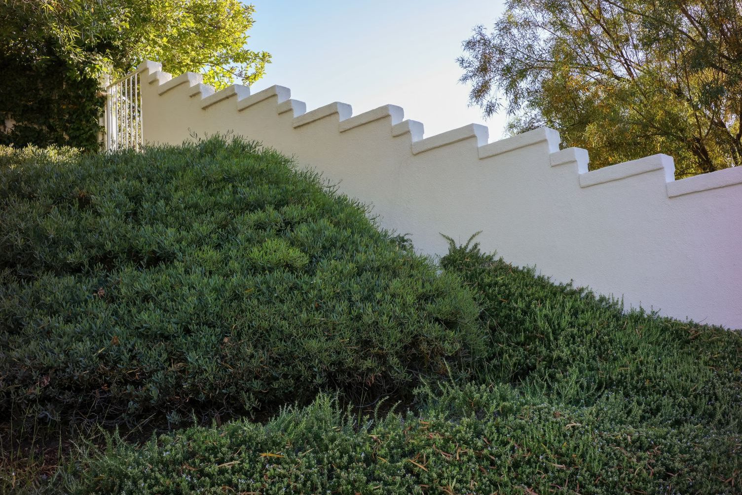 White stone retaining wall terracing a steep hillside, topped by a cable railing