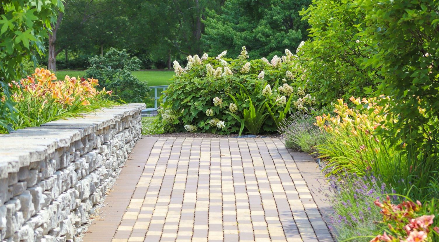 Paver walkway beside a stacked stone retaining wall with flower beds along the edge